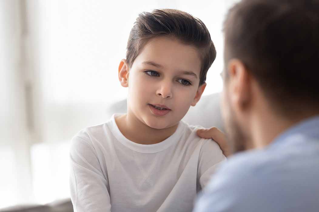 A young boy sits while speaking to his father.